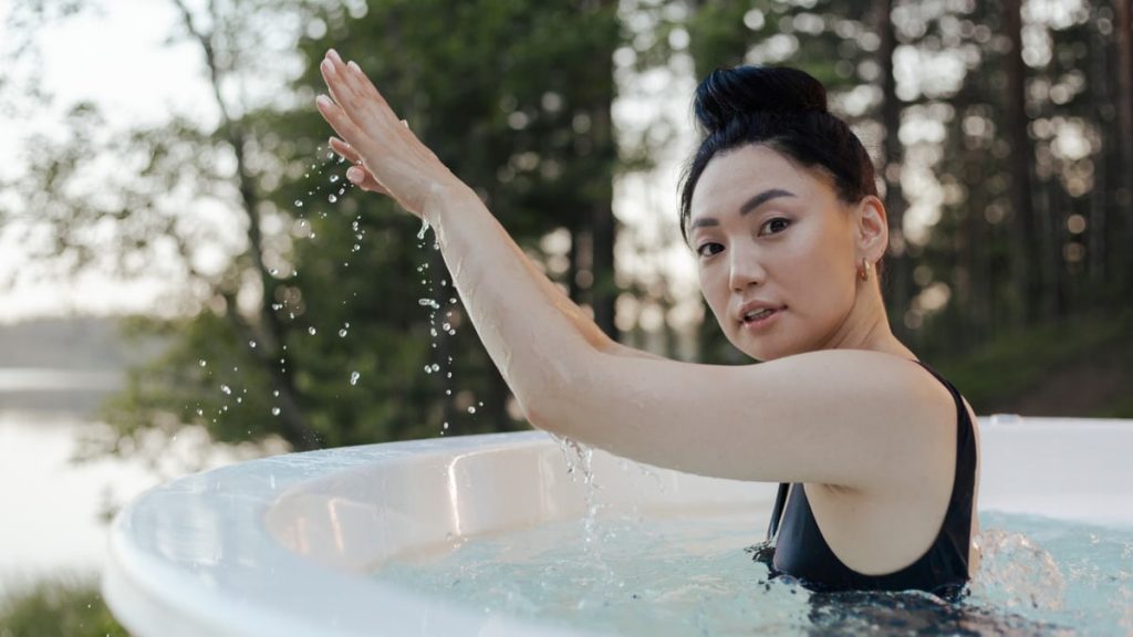 An Asian woman enjoys relaxation in an outdoor hot tub surrounded by nature.
